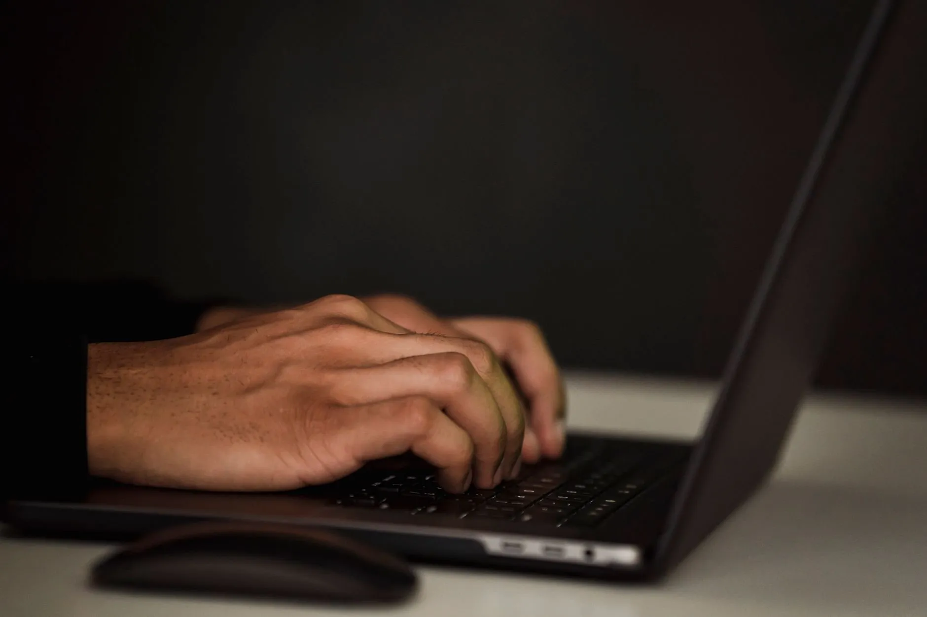 Hands typing on a dark laptop keyboard