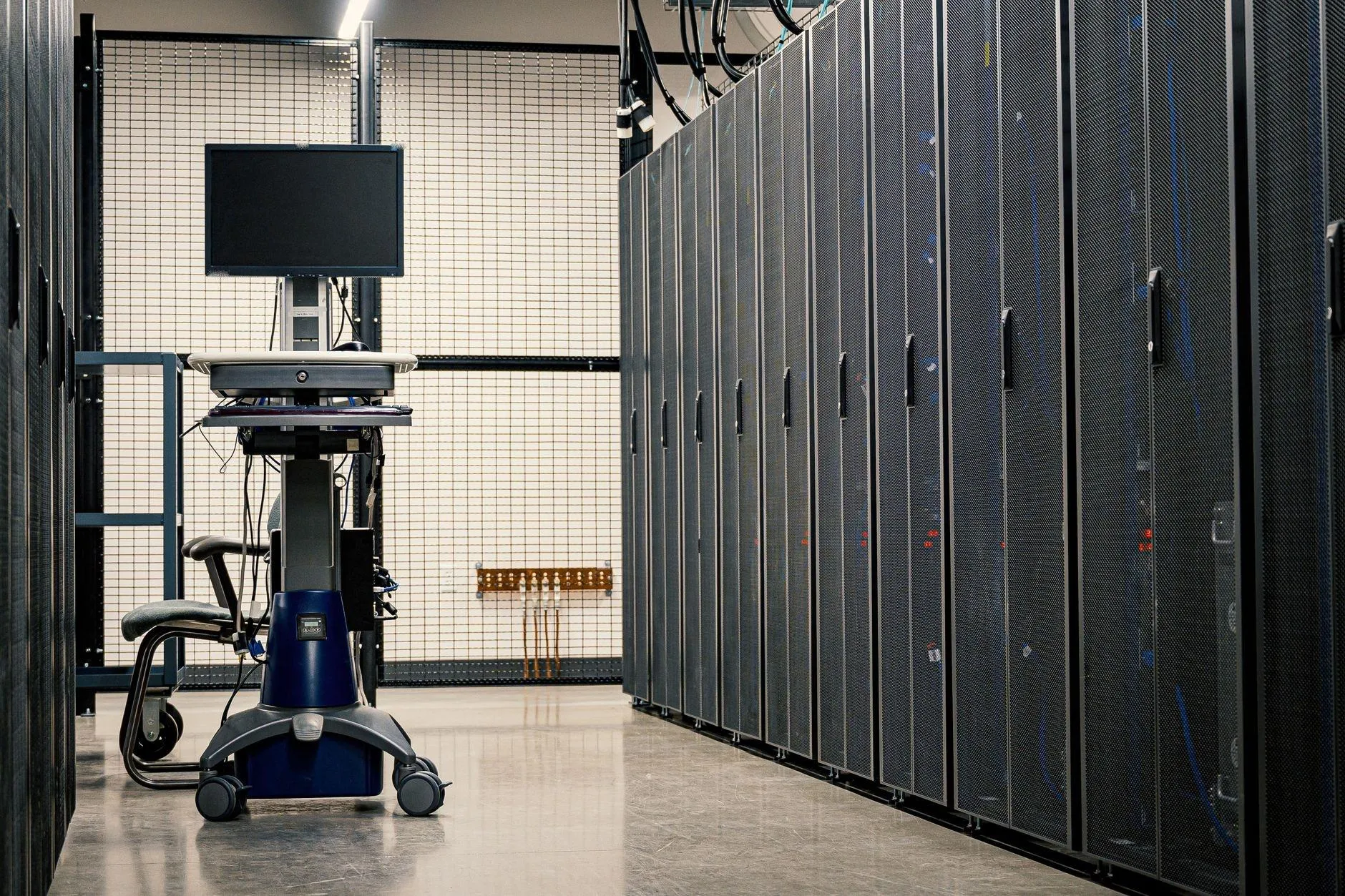 A quiet aisle of black server cabinets with a monitor cart at the far end